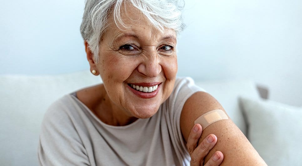 Woman smiling at camera with a bandage on arm after receiving a vaccine